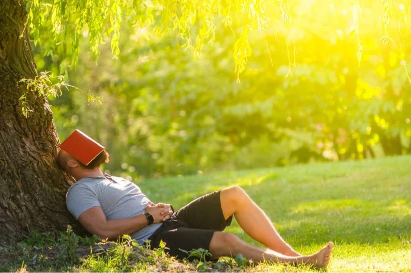 Man lying in the grass and leaning against a tree.