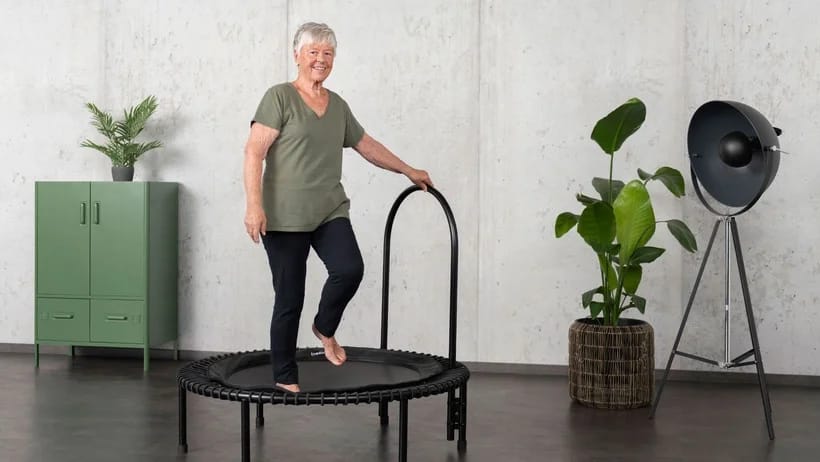 Dame âgée sur le mini trampoline bellicon avec une barre de stabilisation latérale.