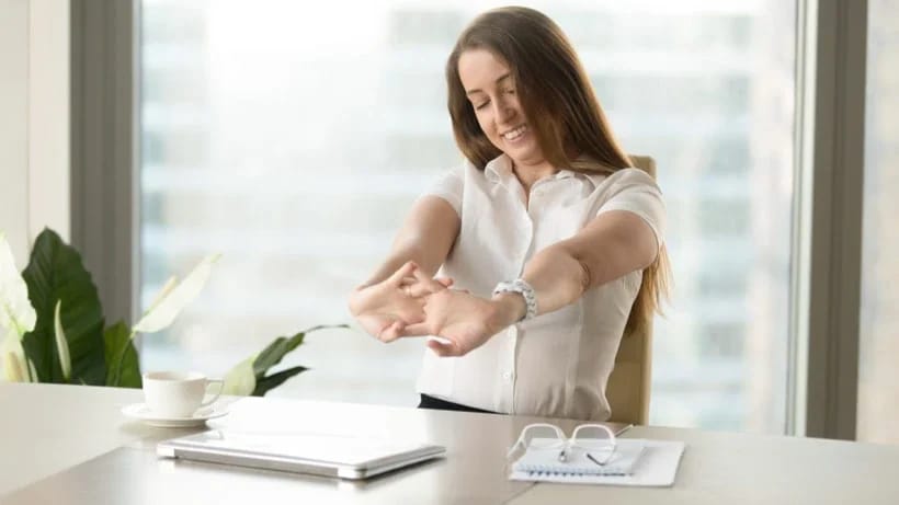 Eine Frau macht eine kurze Dehnübung an ihrem Schreibtisch. 