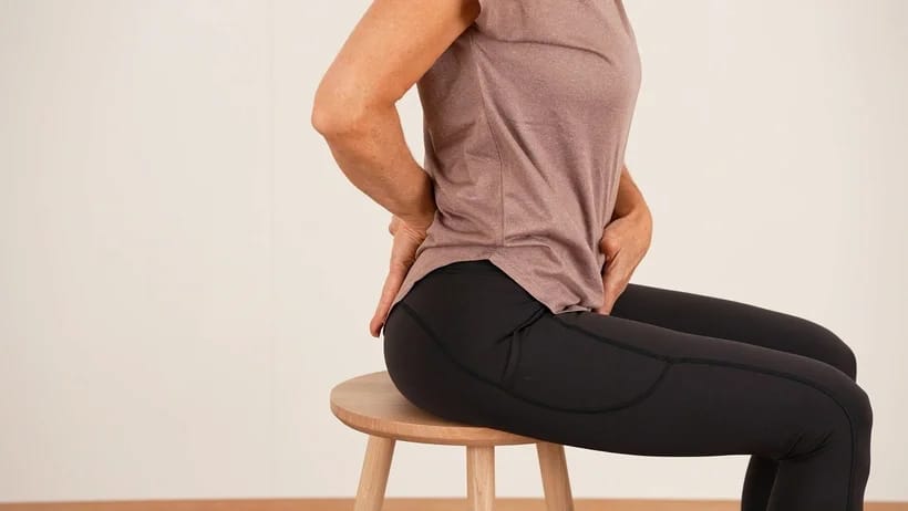 Jacqueline Huber sitzt auf einem Hocker und zeigt die optimale Beckenstellung mit ihren Händen.